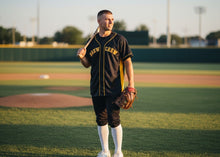 Load image into Gallery viewer, Baseball player holding a bat and glove on a baseball field
